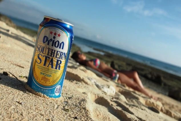 沖縄のビーチで、砂浜に置かれたオリオンビール。リゾートバイトの休日は、青い海を眺めながら、沖縄ならではのビールで乾杯するのも最高です。