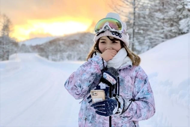 スキー場の雪道で笑顔の女性。カラフルなウェアとゴーグル姿。リゾートバイトの仕事の合間や休日に雪山を満喫。