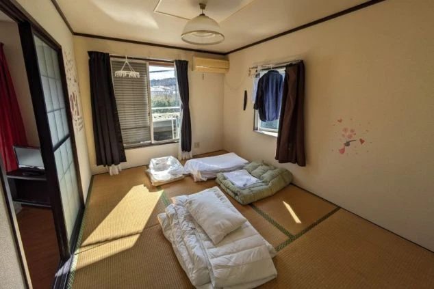 リゾートバイトのシェア寮個室内の様子。畳敷きの部屋に布団が敷かれ、エアコンも完備。プライベート空間が確保された寮付きリゾートバイトで、全国の求人情報をお探しならワクトリへ。