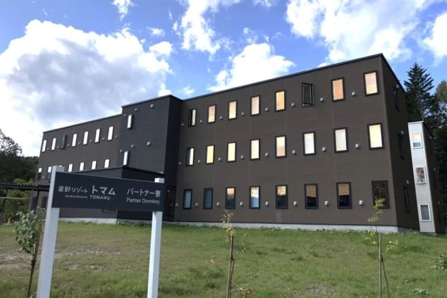 モダンなデザインの黒っぽい建物、寮の外観の画像。多くの窓から光が漏れており、トマムリゾートで働く従業員が住む寮のイメージ。