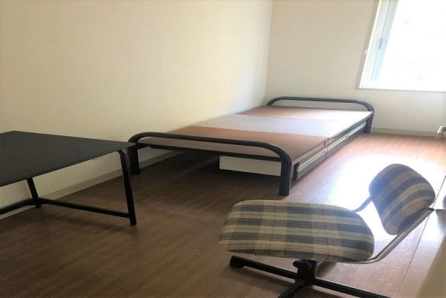 寮の個室画像。窓、カーテン、ベッド、デスク、イスが配置されています。