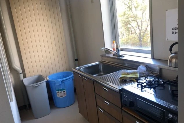 寮の共用キッチンの画像。シンク、ガスコンロ、電子レンジ、大型の冷蔵庫が設置されています。