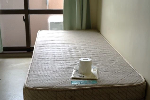 リゾートバイトの寮の部屋の画像。ベッドの上にトイレットペーパーとタオルが置かれ、窓から光が差し込んでいる。シンプルな居住空間。