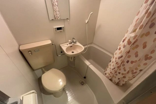 寮のユニットバス。浴槽、洗面台、トイレがコンパクトに一体化した浴室で、浴槽の上には水玉模様のシャワーカーテンが掛かっている。