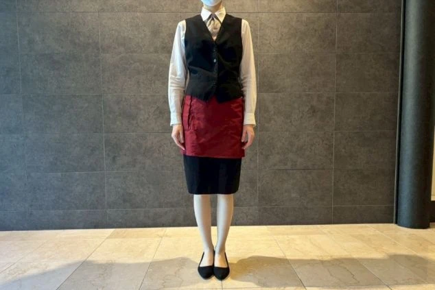 朝食時の制服を着た人物。白いシャツに黒いベストと赤いショートエプロンを着用している。