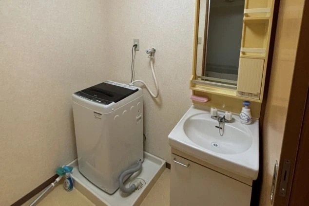 リゾートバイトの個室寮にある洗面所。洗面台の横に洗濯機が置かれており、身だしなみや洗濯に便利な設備の画像。