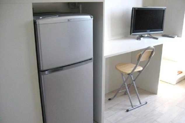 リゾートバイトの寮の部屋の画像。テレビと折りたたみ椅子が置かれ、隣には冷蔵庫が備わっている。
