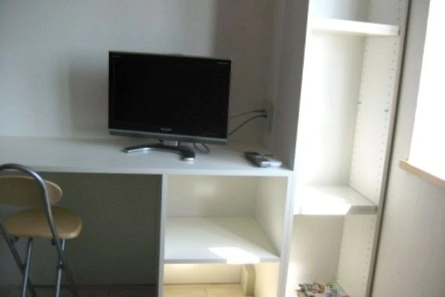 リゾートバイトの寮の部屋のデスク周りの画像。テレビとリモコン、椅子、そして棚が備え付けられている。快適な生活環境を示す。