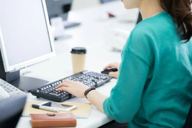 オフィスでデスクワークをする女性。パソコンを操作し、キーボードを打っている。