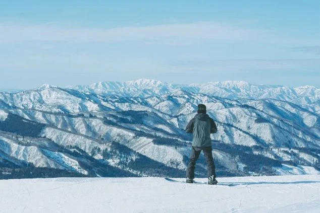  雪に覆われた山々の広大な景色を眺めるスノーボーダーの後ろ姿。