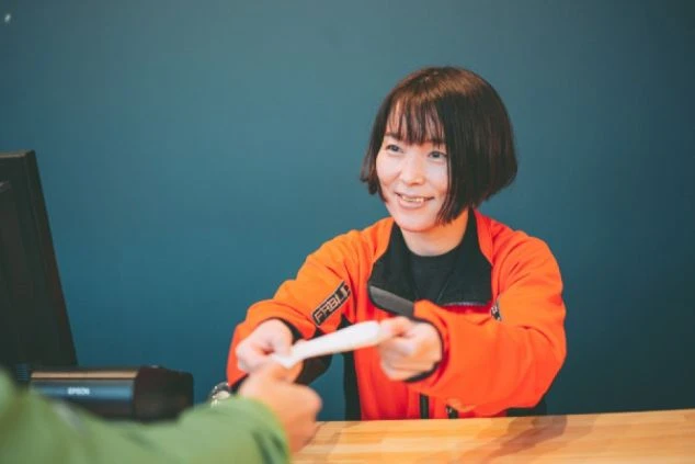 オレンジ色のジャケットを着た女性が、カウンターでチケットを差し出している。