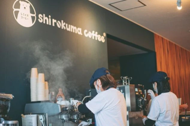 「しろくまコーヒー」と書かれた看板の下で、2人のスタッフがコーヒーを淹れている。エスプレッソマシンからは湯気が立ち上っている。