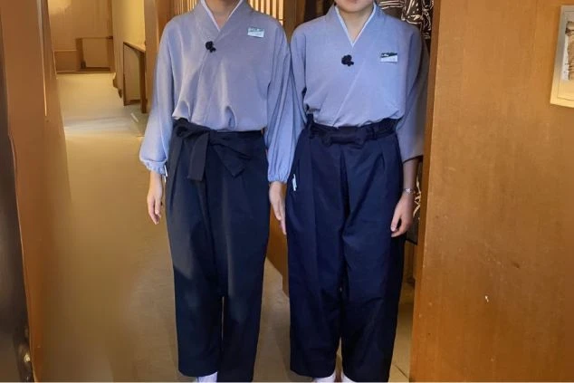 和風の制服を着用した2人の女性スタッフの画像。上下ともゆったりとしたデザインで、グレーの上着に黒い袴のようなズボンを合わせている。旅館や和食レストランでのリゾートバイトの仕事内容を表す、制服の画像。