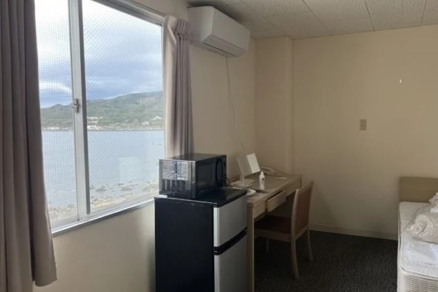 窓から海が見えるリゾートバイト寮の個室。冷蔵庫、電子レンジ、エアコン完備で快適な生活。