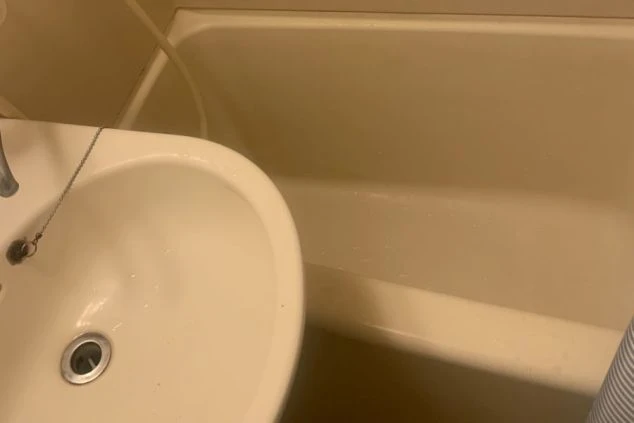 淡いベージュ色の壁と白い陶器のシンクの一部が写っているクローズアップ画像。シンクの縁と壁の間の影が、奥行きを生み出しています。画像は明るく、清潔感のある印象です。