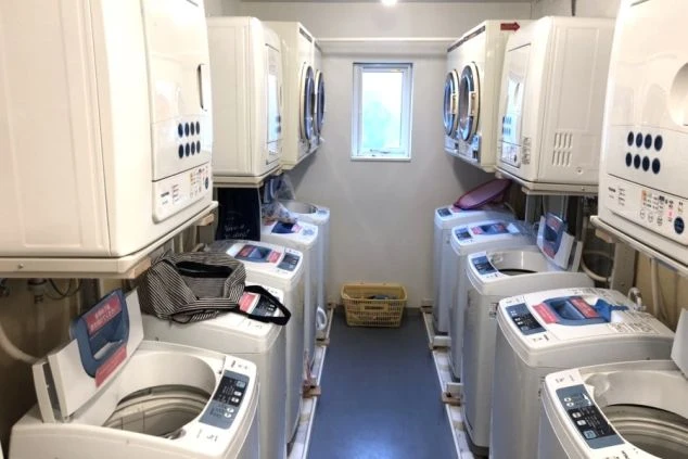 壁沿いに洗濯機と乾燥機が複数台設置された、清潔感のあるランドリールームが写っている画像。リゾートバイトの寮に完備された、スタッフが無料で利用できる共同洗濯室のイメージ。
