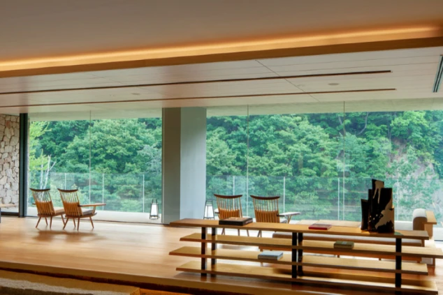 窓の外に緑豊かな木々が見える、広々としたラウンジ。部屋の中央には本棚、窓際には椅子がいくつか置かれている。