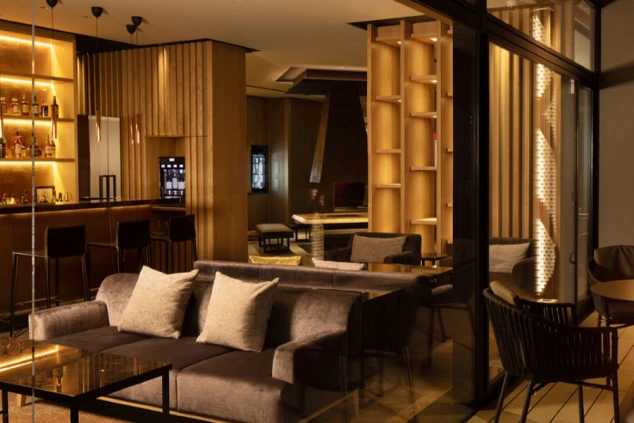 モダンな内装のバー。部屋にはバーカウンター、ソファ、木製の棚があり、暖色系の照明が照らしている。