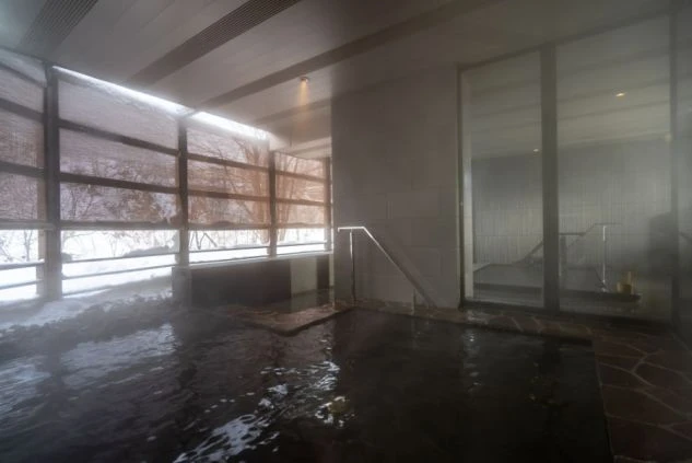 大きな窓から雪景色が見えるモダンな内風呂。湯気が部屋全体に立ち込めている。