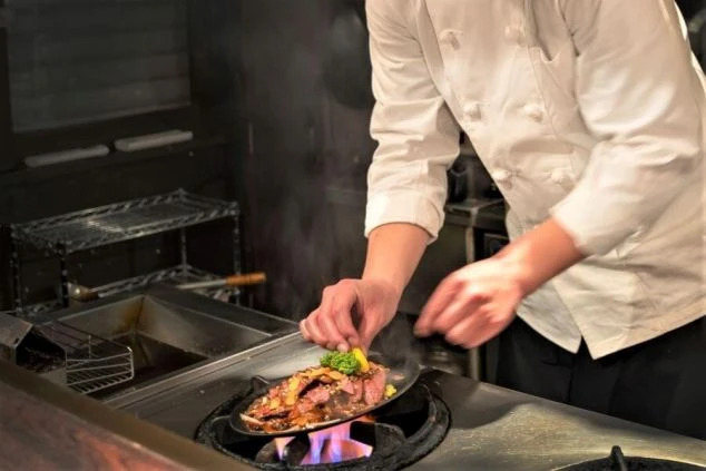 リゾートホテルの厨房で豪華な料理を調理する料理人の写真。調理業務イメージ。