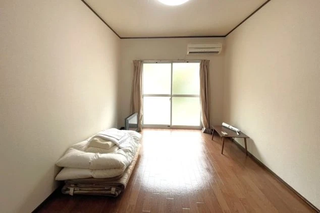 リゾートバイトの寮の個室。日当たりの良いフローリングの部屋で、布団とエアコンが完備されています