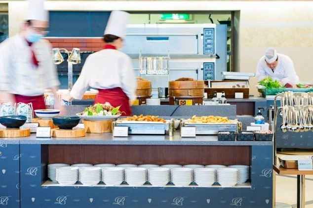 モダンな建物外観。ベージュと濃い色のラインが入った多層階のホテル棟と、エントランス部分のサイン。