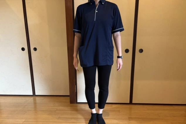 濃紺のポロシャツと黒いパンツを着用した女性スタッフの画像。動きやすく、客室清掃や施設管理などの裏方業務に適した服装である。リゾートバイトの仕事内容を表す、裏方スタッフの制服画像。