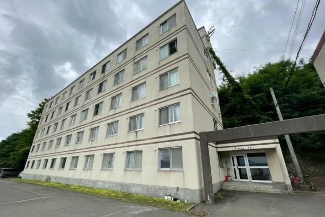 寮の入口。コンクリートの柱とガラスドアで構成されたエントランスで、建物の壁はベージュ色。