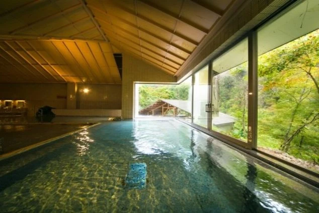 広々とした内湯から窓越しに緑豊かな大自然の景色を眺められる温泉の写真。仕事の疲れを癒したい時にこのような絶景温泉に入れるなど、リゾートバイトの大きな魅力を伝えます。