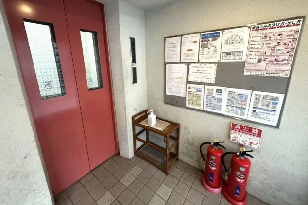 寮のエントランスロビーの画像。エレベーター、掲示板、消毒液が設置された、管理の行き届いた住み込みバイトの共用部。