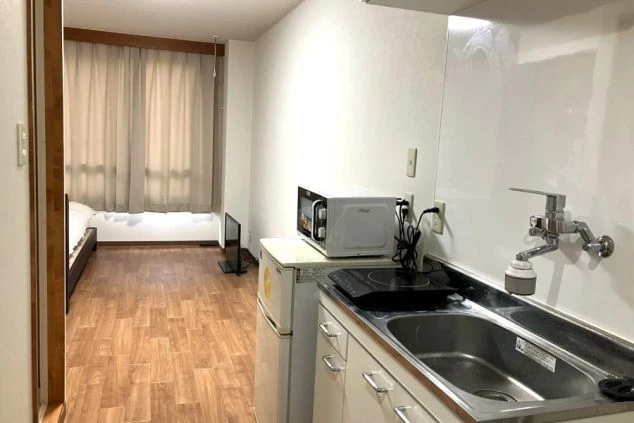 リゾートバイトの個室寮の室内。シングルベッド、テレビ、ミニキッチン、電子レンジが備え付けられた、快適な設備の画像。