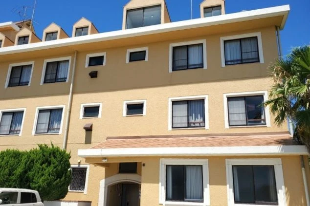 淡路島にある「シーショア慶野松原」のリゾートバイト寮の外観。黄色い建物と南国風のヤシの木が特徴的な、住み込み生活の雰囲気が伝わる画像。