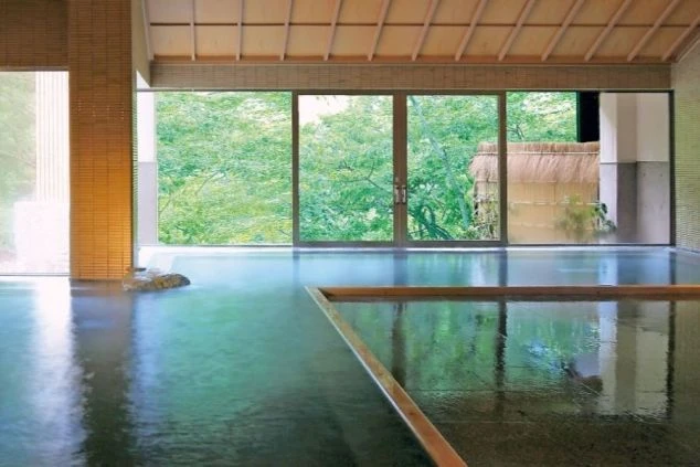 広々とした内湯から、窓越しに緑豊かな大自然の景色を眺められる温泉の写真。仕事の疲れを癒したい時に、このような絶景温泉に入れるなど、リゾートバイトの大きな魅力を伝えます。