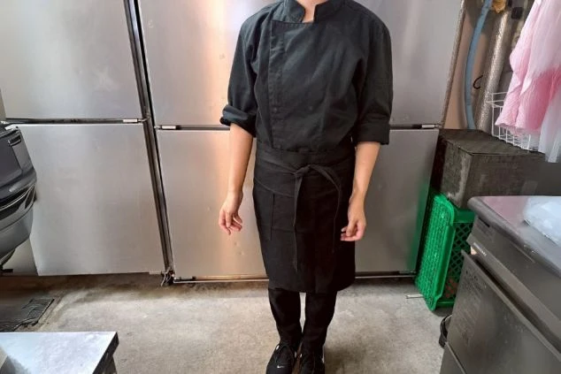 黒いコックコートとエプロン、パンツを着用した、調理補助スタッフの制服。リゾートバイトでキッチン業務に興味がある方に、仕事内容をイメージさせる画像。