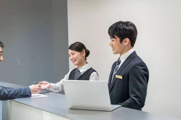 ホテルのフロントで、宿泊客と笑顔で話すリゾートバイトの男女スタッフの画像。