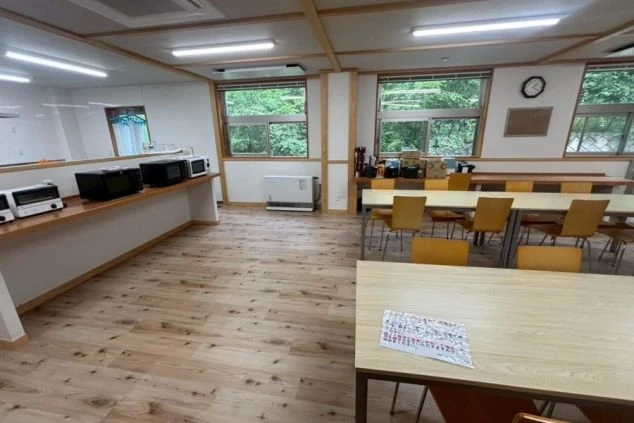 リゾートバイトの従業員寮の玄関の画像。床には茶色のタイルカーペットが敷かれており、壁際には備え付けの棚と冷蔵庫が置かれている画像。