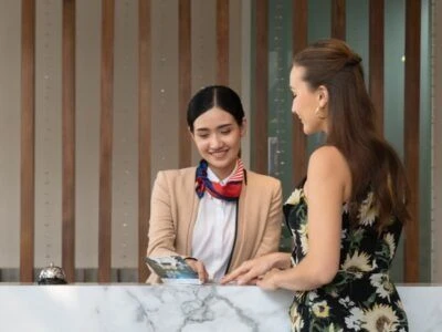 ホテルのフロントの画像。制服を着た女性スタッフが、チェックインするお客様を笑顔で案内している画像。