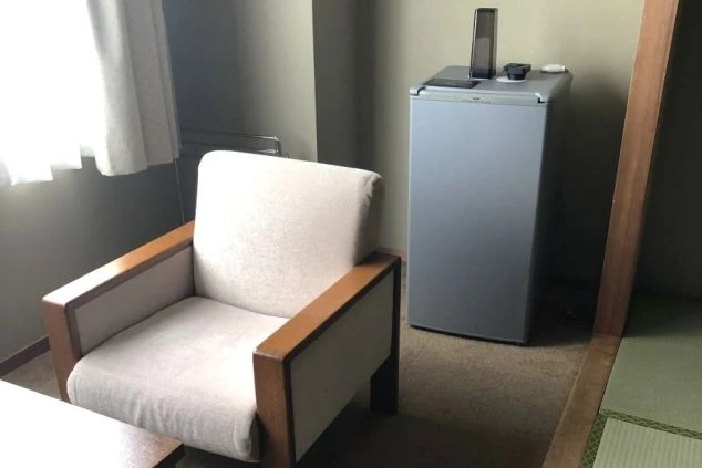 リゾートバイトの寮の部屋にある、一人掛けのソファと冷蔵庫の画像。ソファは落ち着いた色合いで、リラックスできる。リゾートバイトの寮の部屋の画像。