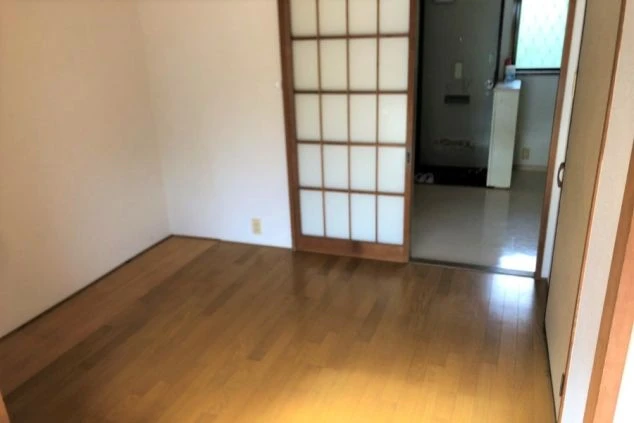 寮の個室。和室からキッチンへ続く、障子と冷蔵庫、コンロがある部屋が映る。