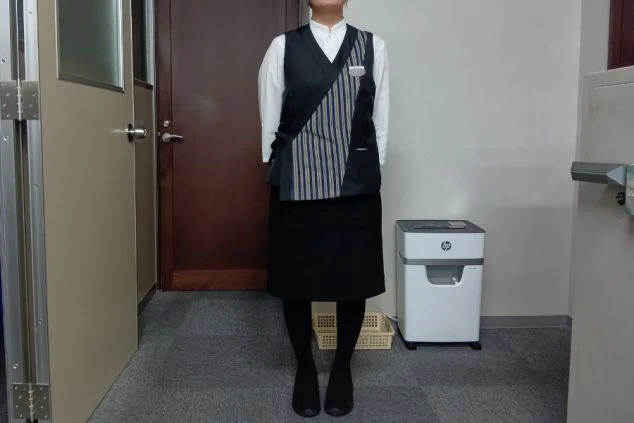 白いブラウスに黒いスカート、和風のデザインが施されたベストを着用した、ホテルの女性フロントスタッフの制服。落ち着いた雰囲気の旅館やホテルでのリゾートバイトを検討している方に魅力的な画像。