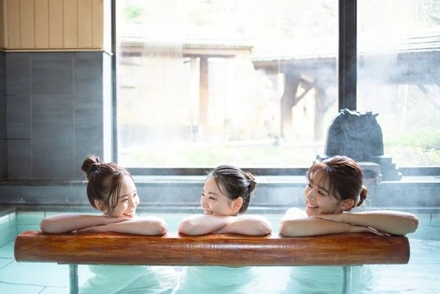 温泉に浸かりながら笑顔で談笑する3人の女性。リゾートバイトで温泉地での仕事と、仕事の後に温泉を楽しめる魅力を伝える画像。