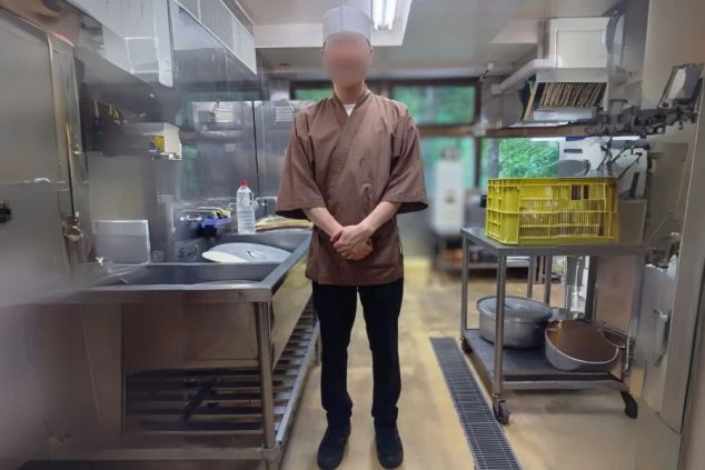 茶色の上着と黒いパンツを着用し、コック帽を被った調理スタッフの制服。リゾートバイトで調理や洗い場業務に興味がある方に、仕事内容をイメージさせる画像。