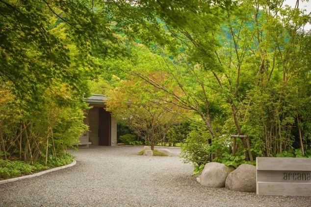 緑の木々に囲まれた敷地のエントランス。砂利が敷かれた道が建物へと続いている。