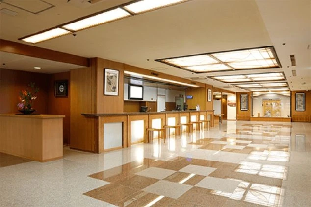 大規模な旅館またはホテルのエントランス。大きな庇の下にガラスの自動ドアがあり、旅館の名前が書かれた看板や案内が見える。建物の側壁には立派な松の木が植えられている。