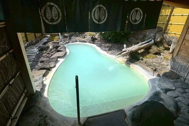 乳白色の湯が特徴的な白骨温泉の露天風呂。大きな岩が配置され、リゾートバイトで温泉旅館のスタッフとして働きながら、温泉を楽しめることを示す画像。