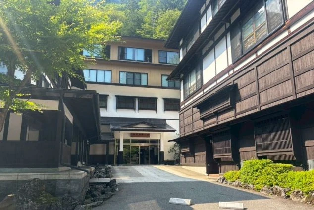 和風の趣ある建物とモダンな建物が一体となった、温泉旅館の外観。山間に位置し、リゾートバイトで温泉地での仕事に興味がある方に訴求する画像。