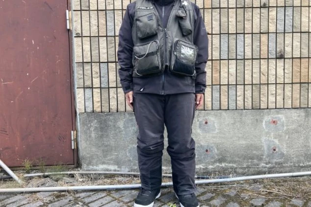 ゲレンデパトロールの制服を着た男性。黒いジャケットの上に、たくさんのポケットがついたグレーのベストを着用している。