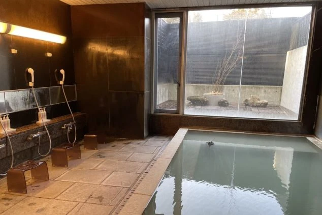 黒いタイル張りのモダンな大浴場。シャワーと洗い場があり、湯船の横の窓からは中庭が見える。