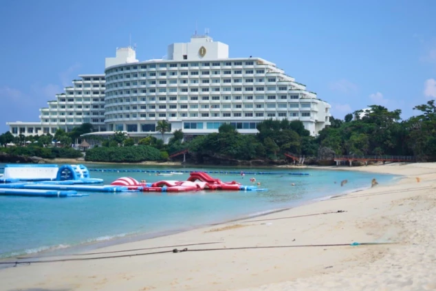白い大型ホテルとエメラルドグリーンの海、砂浜、海上アスレチック。