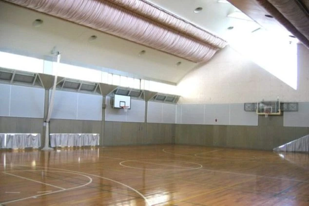 木の床のバスケットボールコートがある体育館。部屋の壁には白いパネルが取り付けられている。